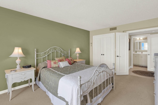 carpeted bedroom with ensuite bathroom and a textured ceiling