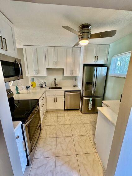 kitchen with light tile patterned flooring, sink, white cabinetry, ceiling fan, and stainless steel appliances