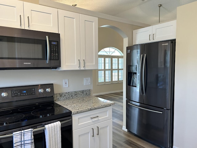 kitchen featuring appliances with stainless steel finishes, a textured ceiling, light stone countertops, white cabinetry, and wood-type flooring