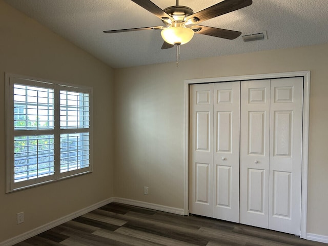 unfurnished bedroom featuring a closet, vaulted ceiling, a textured ceiling, dark wood-type flooring, and ceiling fan