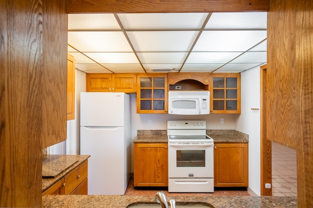 kitchen featuring white appliances, dark stone countertops, a drop ceiling, and sink