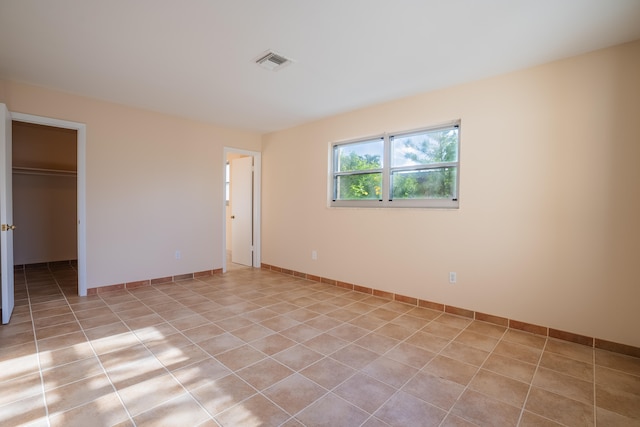 unfurnished bedroom featuring a walk in closet, light tile patterned floors, and a closet