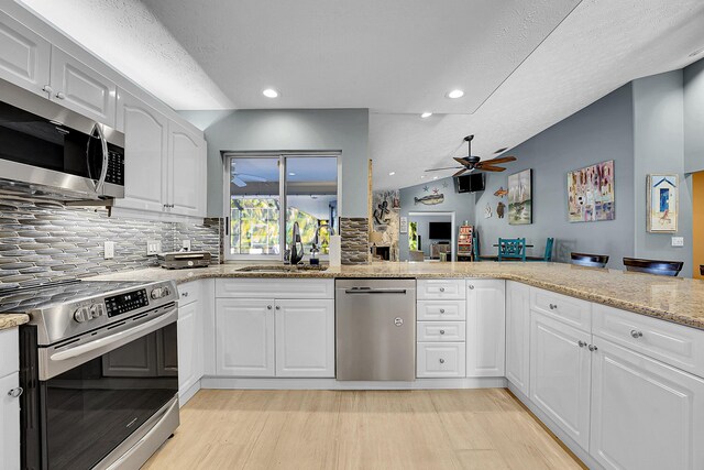 kitchen with sink, white cabinets, kitchen peninsula, stainless steel appliances, and light stone countertops