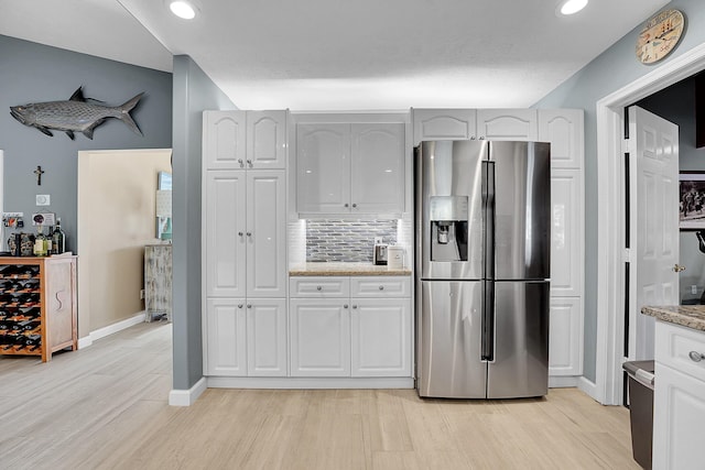 kitchen featuring light hardwood / wood-style flooring, white cabinetry, stainless steel refrigerator with ice dispenser, light stone counters, and decorative backsplash