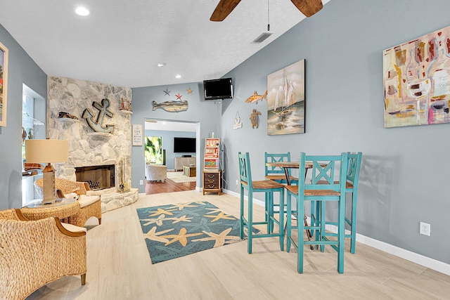 dining area with a stone fireplace, a textured ceiling, ceiling fan, and hardwood / wood-style flooring