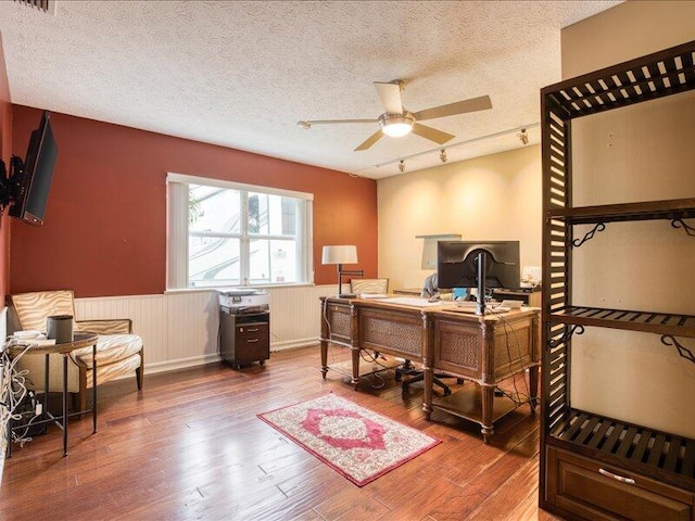 office with wood-type flooring, rail lighting, ceiling fan, and a textured ceiling