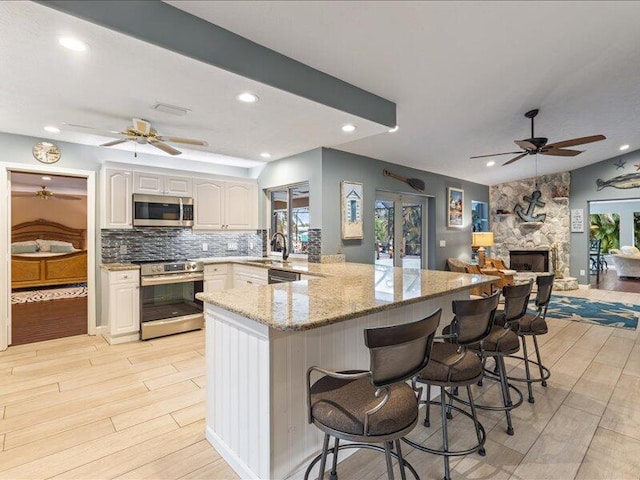 kitchen featuring a breakfast bar area, stainless steel appliances, tasteful backsplash, white cabinets, and light wood-type flooring