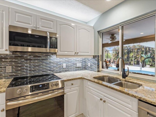 kitchen with appliances with stainless steel finishes, white cabinetry, sink, decorative backsplash, and light stone countertops