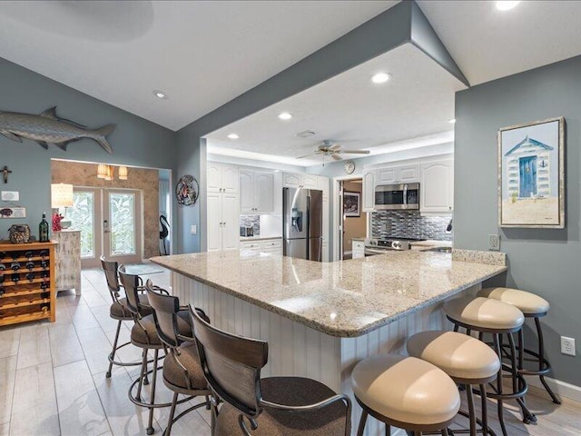 kitchen with a breakfast bar area, white cabinets, kitchen peninsula, stainless steel appliances, and french doors