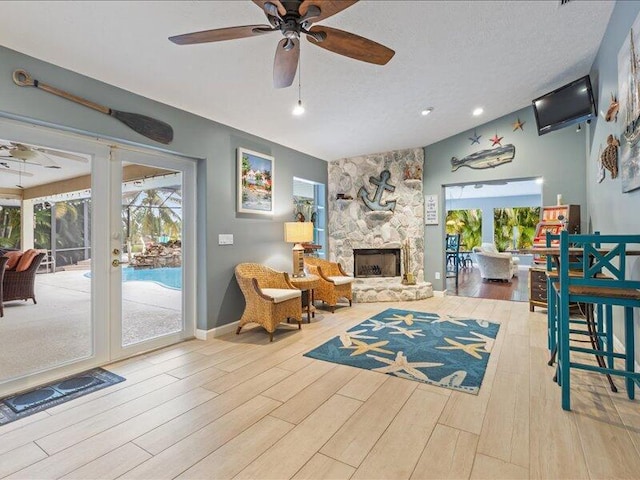 living room featuring ceiling fan, wood-type flooring, a textured ceiling, a stone fireplace, and vaulted ceiling