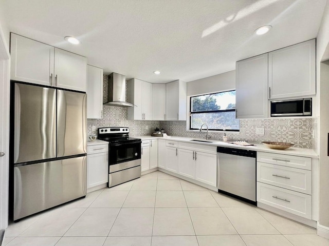 kitchen with white cabinets, stainless steel appliances, light countertops, wall chimney range hood, and a sink