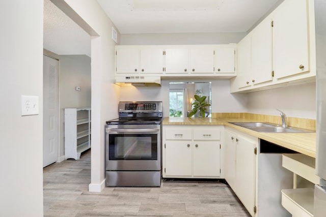 kitchen with stainless steel electric range oven, sink, white cabinetry, light hardwood / wood-style floors, and wall chimney range hood