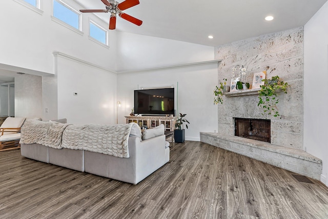 living room with hardwood / wood-style floors, a large fireplace, ceiling fan, and a high ceiling