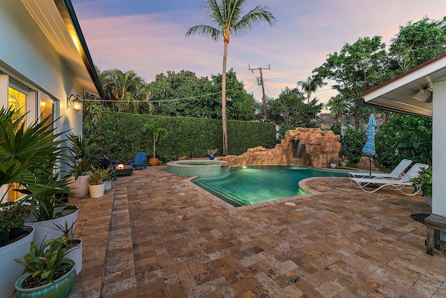 pool at dusk with a patio area, pool water feature, and an in ground hot tub