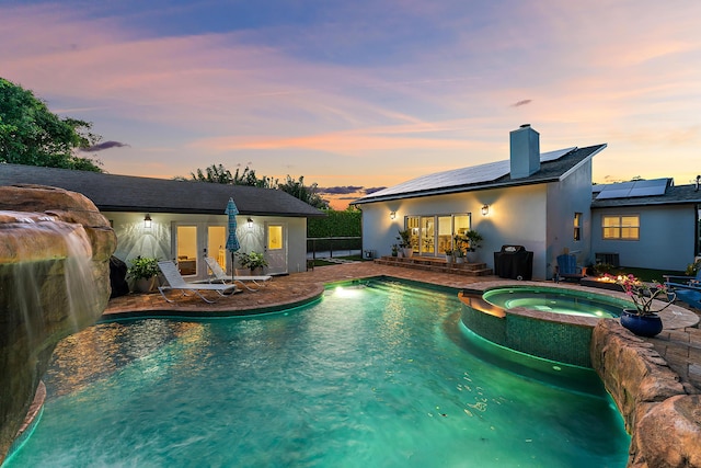 pool at dusk featuring an in ground hot tub, pool water feature, and a patio area