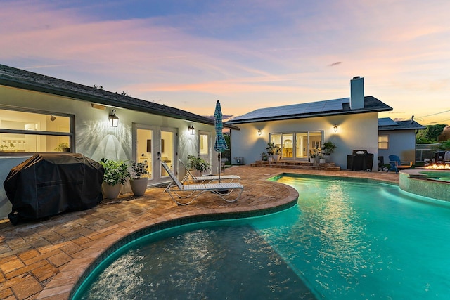 pool at dusk featuring a patio area, grilling area, french doors, and an in ground hot tub