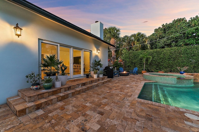 pool at dusk with an in ground hot tub, area for grilling, and a patio area