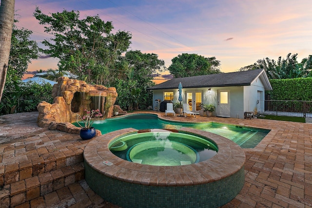 pool at dusk featuring an in ground hot tub, an outbuilding, and a patio area