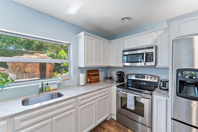 kitchen with appliances with stainless steel finishes, light stone countertops, sink, and white cabinets