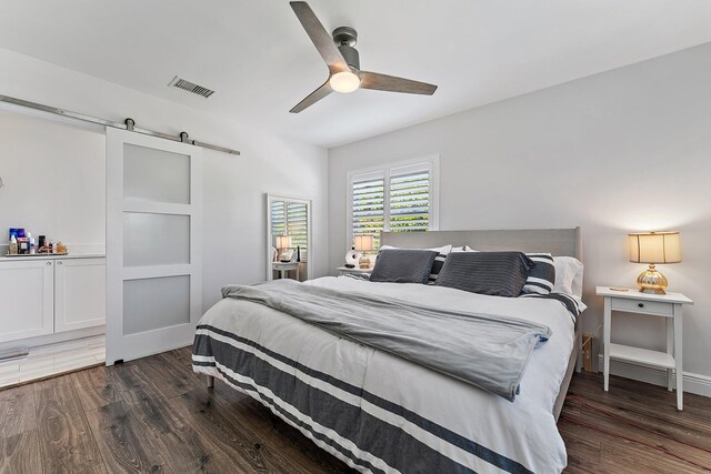 bedroom with dark wood-type flooring, a barn door, and ceiling fan