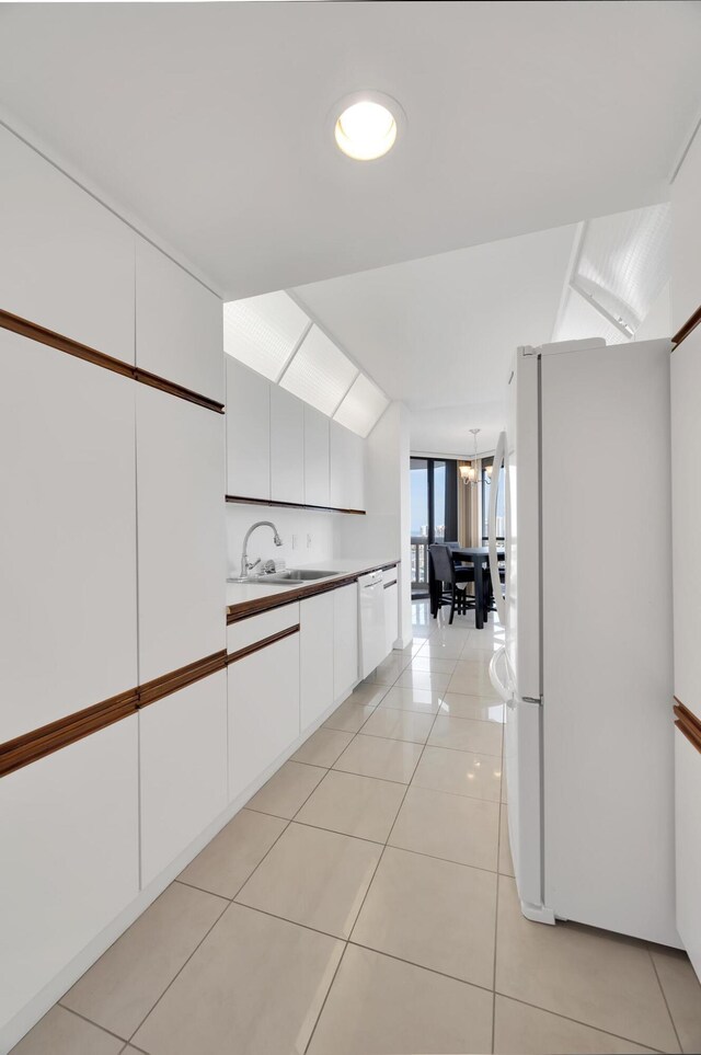 kitchen with a chandelier, light tile patterned flooring, white appliances, a sink, and white cabinetry