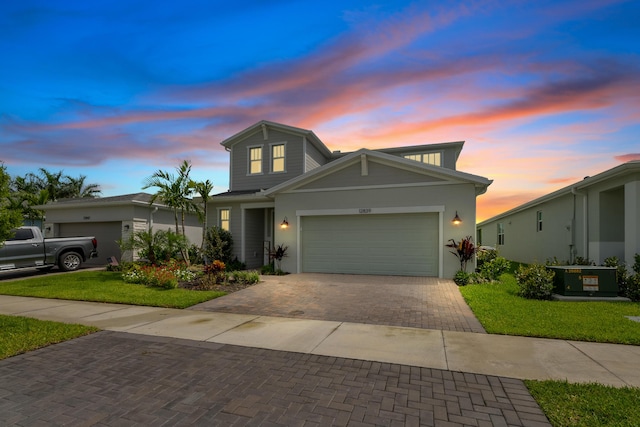 traditional-style home featuring an attached garage, central AC unit, decorative driveway, and a yard