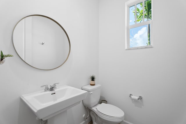 half bath with toilet, baseboards, and a sink