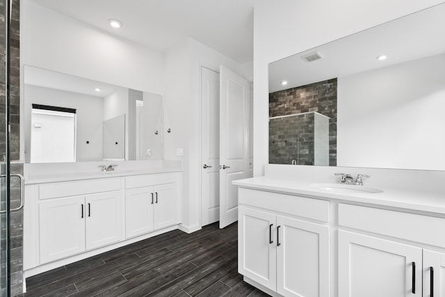 full bathroom featuring two vanities, visible vents, a sink, a shower stall, and wood finished floors