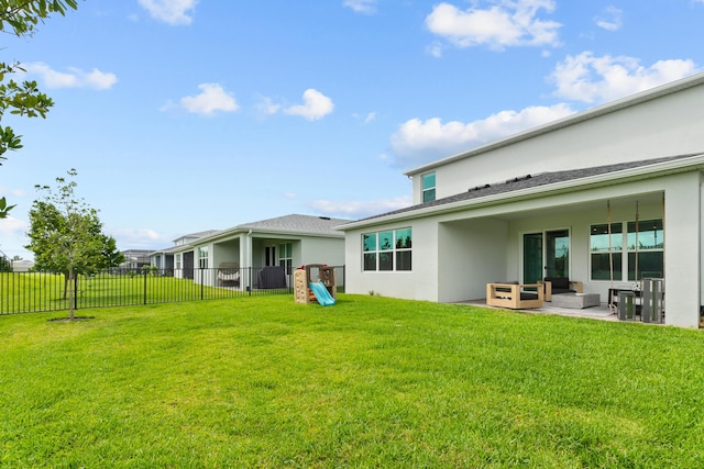 rear view of property with a patio, a playground, fence, a lawn, and stucco siding