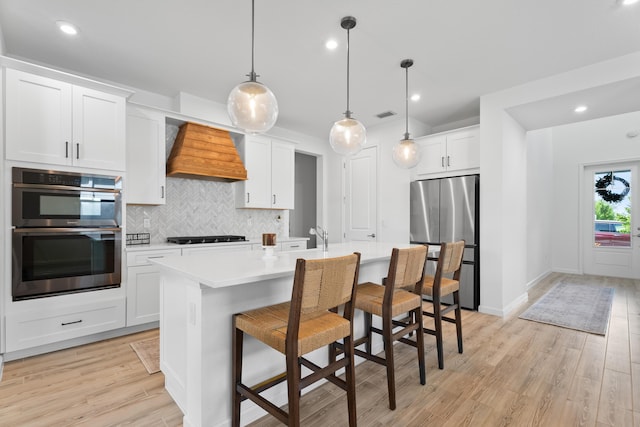 kitchen with white cabinets, an island with sink, appliances with stainless steel finishes, light countertops, and premium range hood