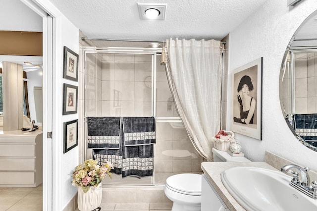 bathroom with tile patterned flooring, a shower with door, a textured ceiling, toilet, and vanity