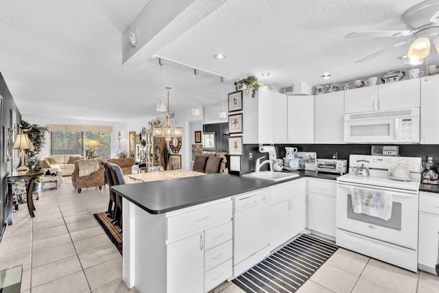 kitchen with ceiling fan with notable chandelier, white appliances, kitchen peninsula, white cabinets, and track lighting