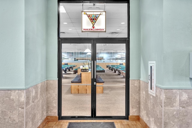 interior space with light wood-type flooring, a drop ceiling, and french doors