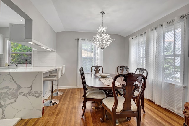 dining room featuring an inviting chandelier, sink, light hardwood / wood-style flooring, and lofted ceiling