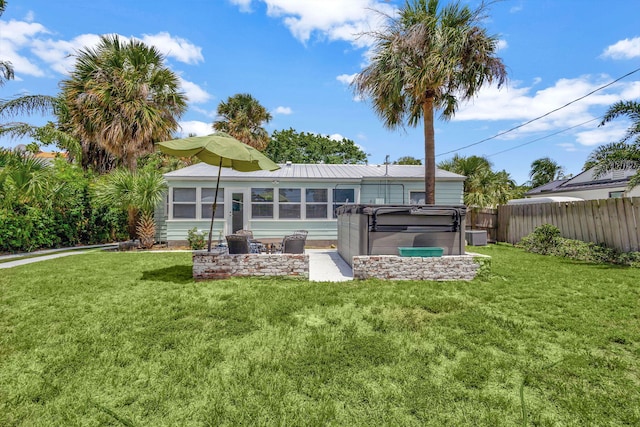 rear view of house featuring a hot tub and a lawn