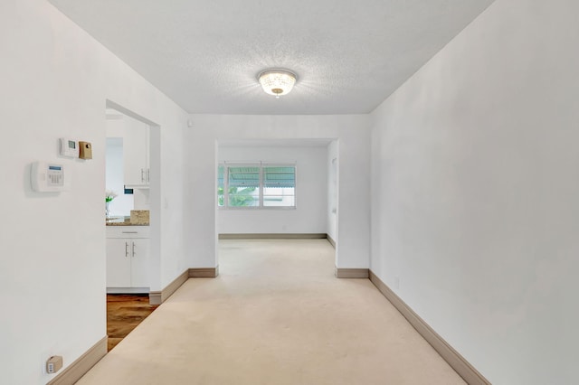 hallway with light wood-type flooring and a textured ceiling