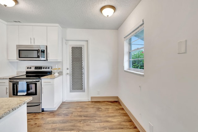 kitchen featuring white cabinetry, stainless steel appliances, light stone countertops, a textured ceiling, and light wood-type flooring