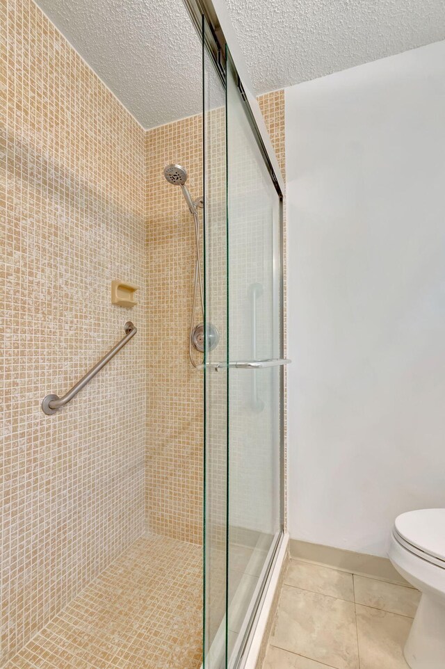 bathroom featuring walk in shower, a textured ceiling, toilet, and tile patterned floors