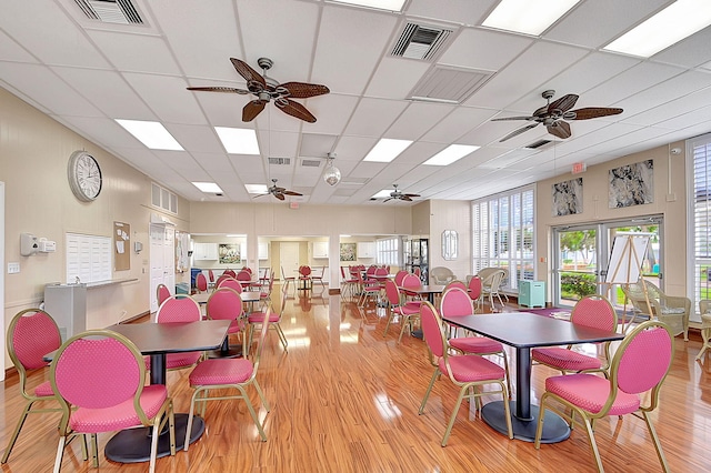 dining area with a paneled ceiling, ceiling fan, and light hardwood / wood-style flooring