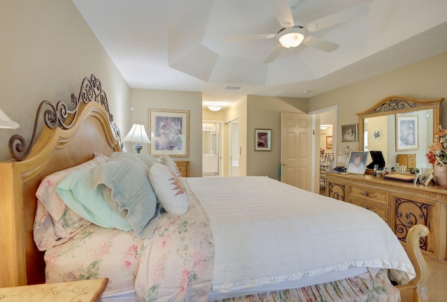 bedroom with a textured ceiling, ceiling fan, ensuite bathroom, and a tray ceiling