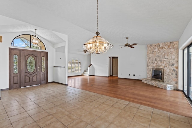 foyer featuring lofted ceiling, light hardwood / wood-style floors, a stone fireplace, a textured ceiling, and ceiling fan with notable chandelier