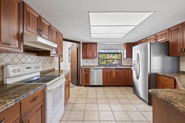 kitchen featuring appliances with stainless steel finishes, tasteful backsplash, dark stone counters, and light tile patterned floors