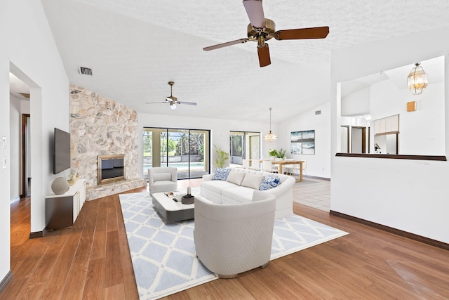 living room featuring a stone fireplace, a textured ceiling, hardwood / wood-style flooring, and vaulted ceiling