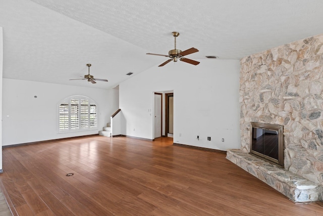 unfurnished living room featuring ceiling fan, a textured ceiling, hardwood / wood-style flooring, high vaulted ceiling, and a stone fireplace