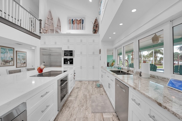 kitchen with black appliances, sink, light hardwood / wood-style flooring, light stone counters, and white cabinetry