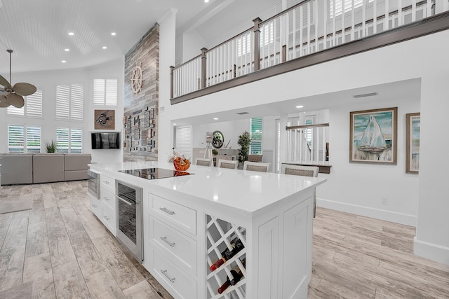 kitchen with a center island, stainless steel oven, a high ceiling, black electric cooktop, and white cabinetry