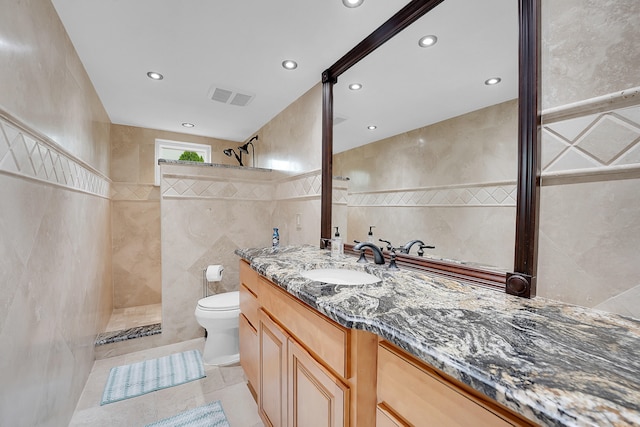 bathroom featuring tile patterned floors, vanity, a shower, tile walls, and toilet