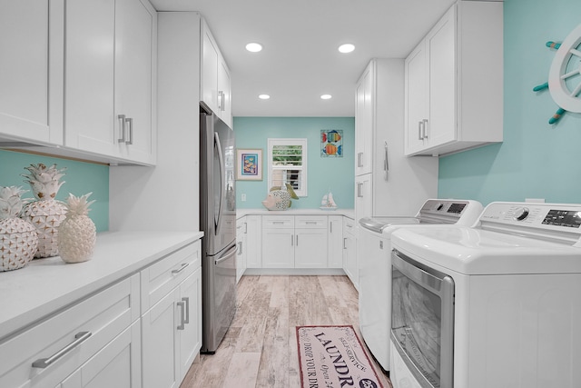 laundry area featuring cabinets, washing machine and dryer, and light hardwood / wood-style floors