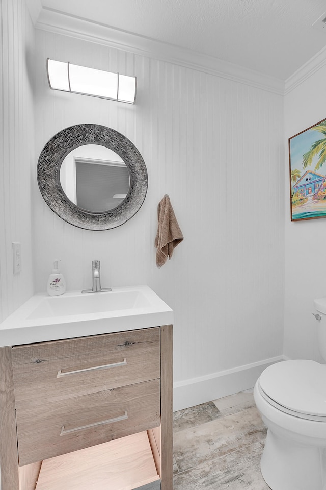 bathroom featuring wood walls, toilet, vanity, and ornamental molding