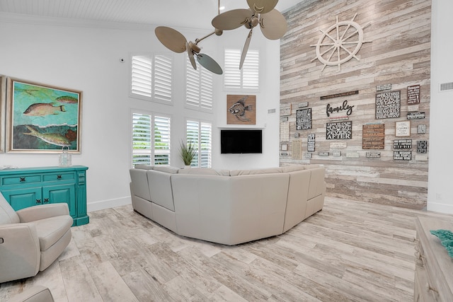 living room featuring a towering ceiling, light wood-type flooring, ceiling fan, and crown molding